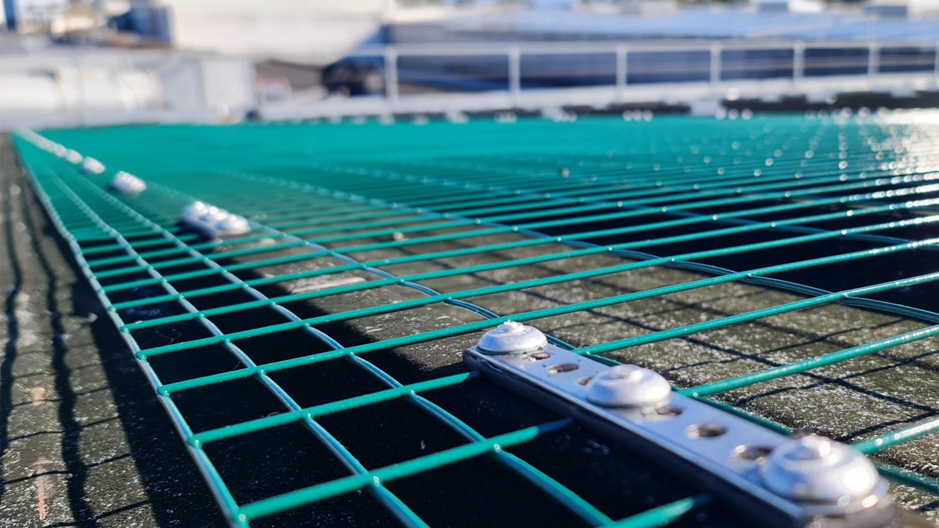 Green safety net installed on a rooftop with secure fastening system.