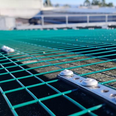 Green safety net installed on a rooftop with secure fastening system. 