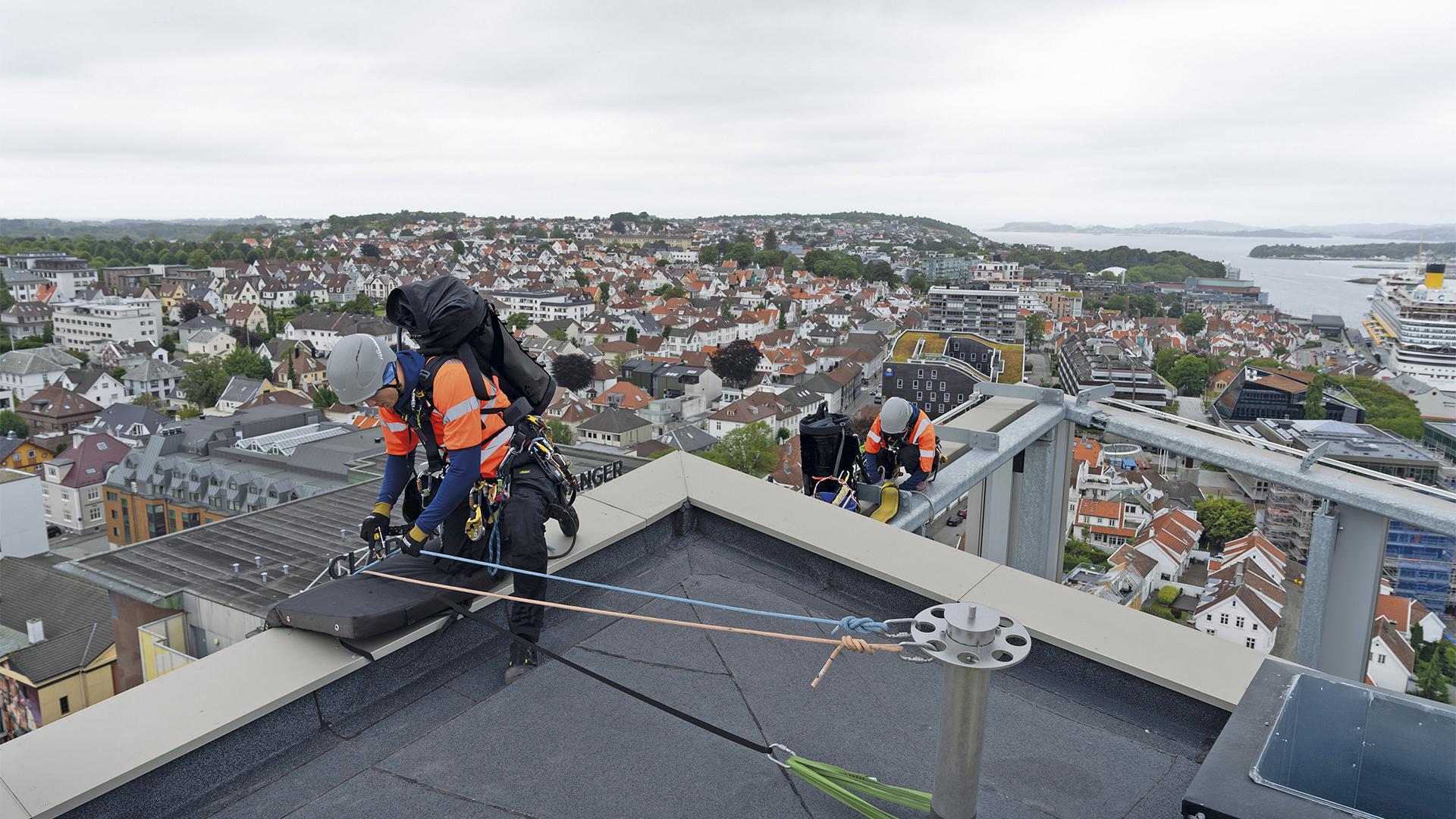 Workers performing anchorage operations on a multi-storey building roof, wearing Rothoblaas HERO safety helmets and fall protection systems