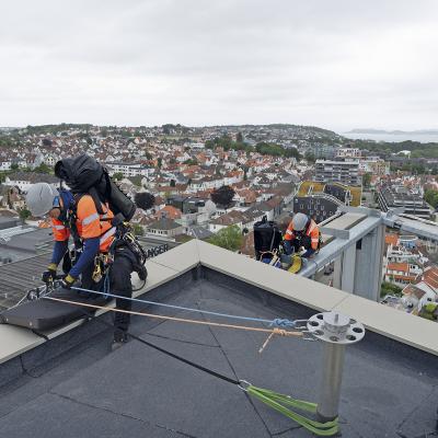 Workers performing anchorage operations on a multi-storey building roof, wearing Rothoblaas HERO safety helmets and fall protection systems