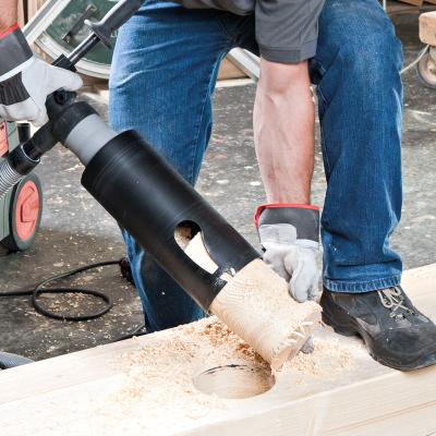Professional woodworking machine drilling a large hole in a timber beam using a wood cutter tool, producing wood chips during structural timber processing