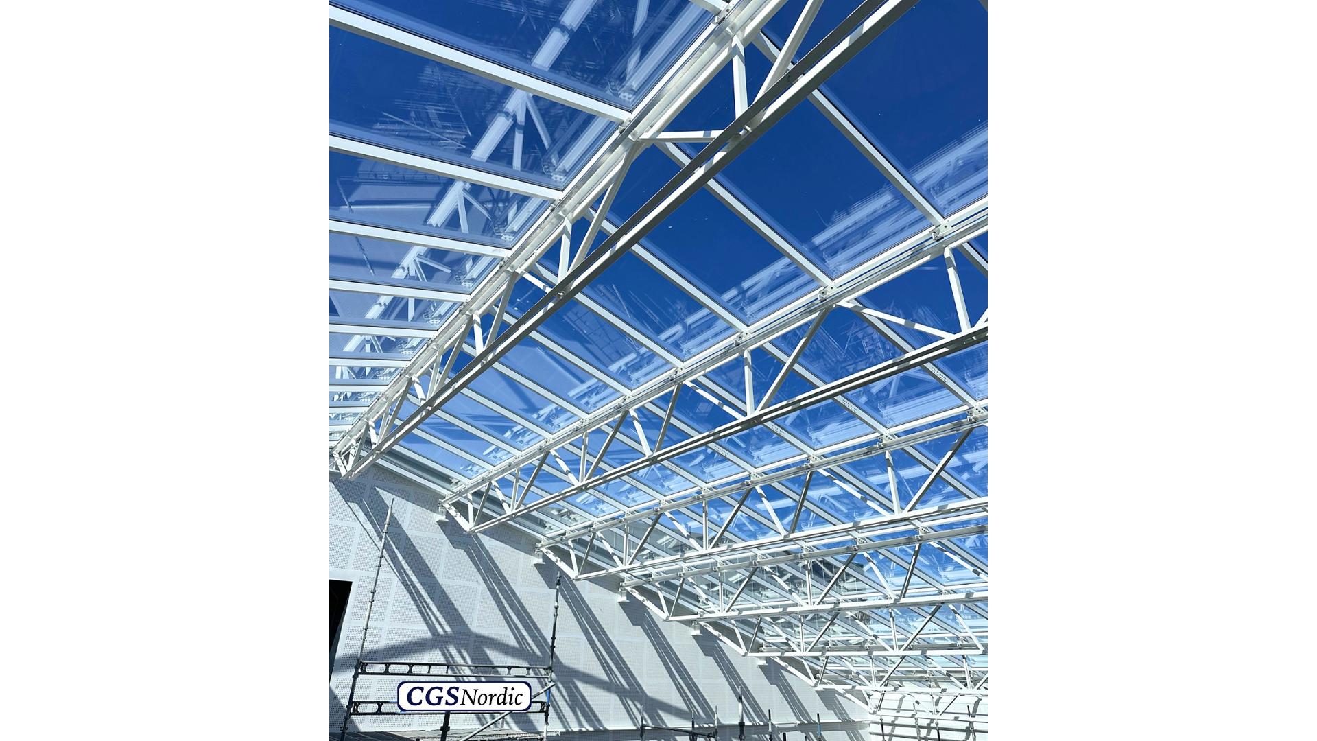 CGS Nordic technician wearing a white safety helmet and gloves, preparing H-RAIL rail components before installation in a glazed building atrium.