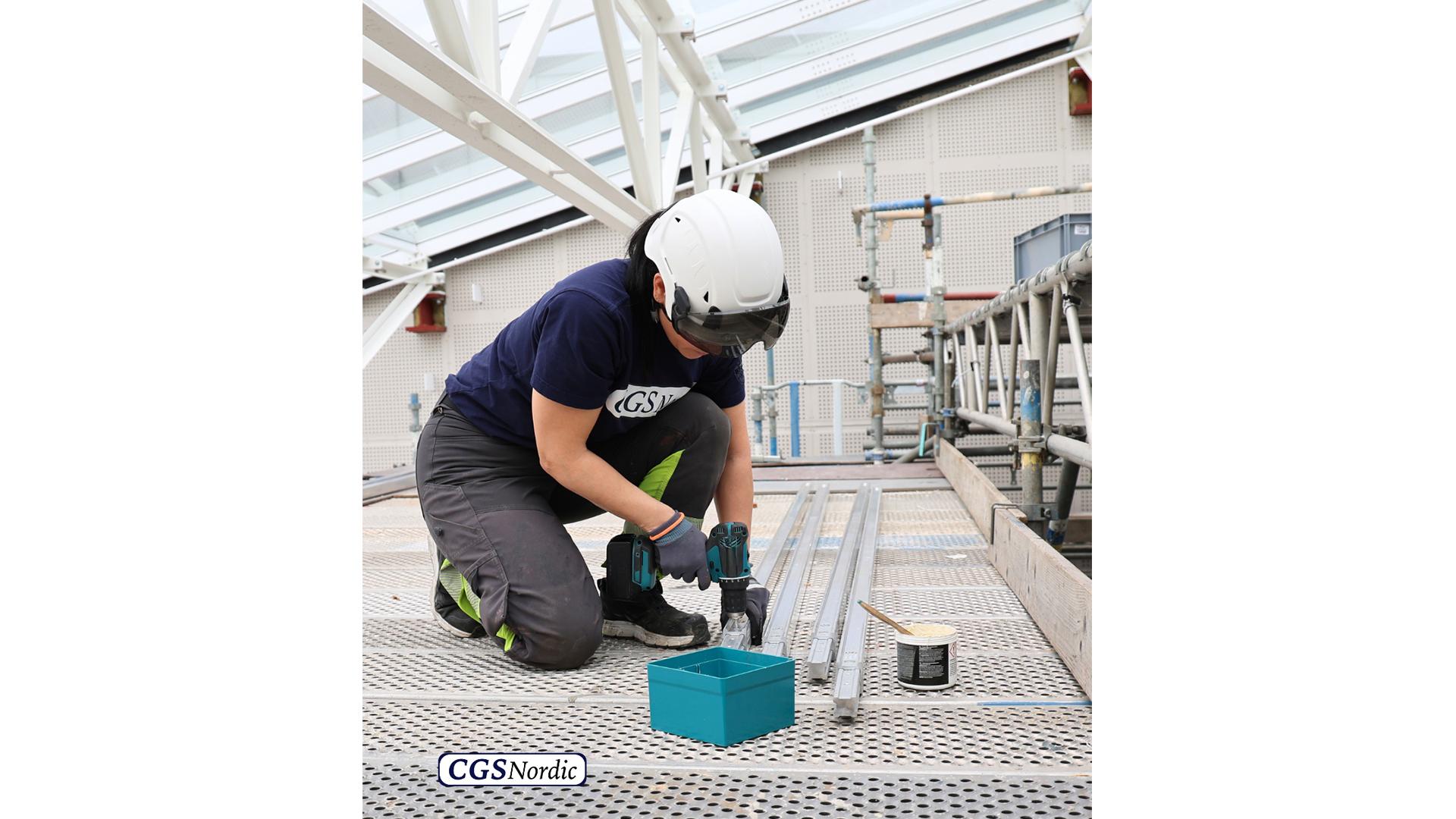 Rope access technician in safety harness suspended from H-RAIL system, working alongside the glazed wall of a building atrium for maintenance and inspection.