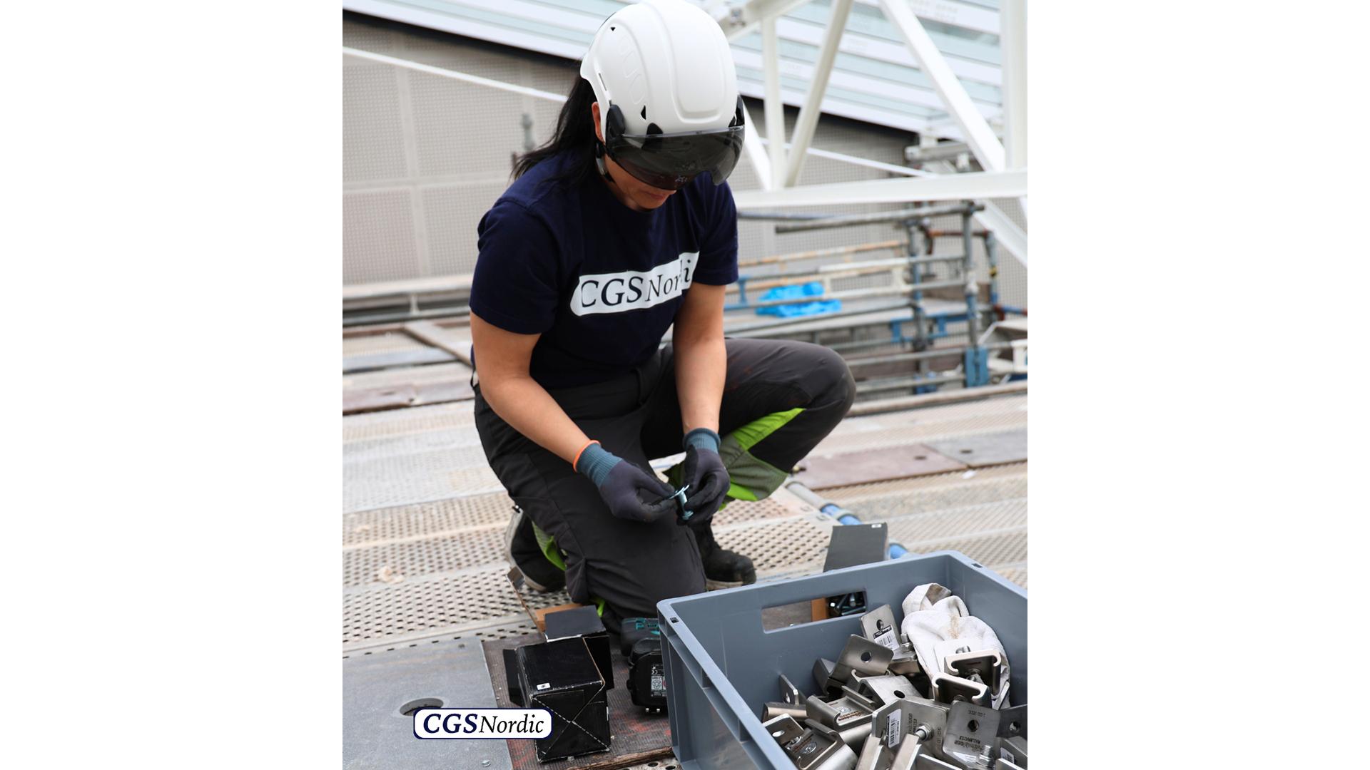 Full body view of a rope access technician in complete safety equipment suspended from H-RAIL system inside a glazed atrium, performing maintenance work at height.
