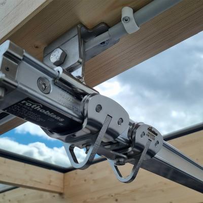 Rothoblaas H-RAIL rigid fall arrest rail system mounted on a glulam timber beam — sliding runner detail on a large-span timber and glass roof structure, Denmark.