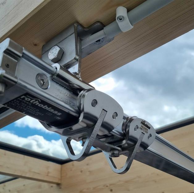 Rothoblaas H-RAIL rigid fall arrest rail system mounted on a glulam timber beam — sliding runner detail on a large-span timber and glass roof structure, Denmark.