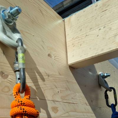 Rothoblaas WING single anchor points installed on a glulam timber beam junction — rope access carabiners and ropes connected for suspended work below a timber roof structure, Denmark.